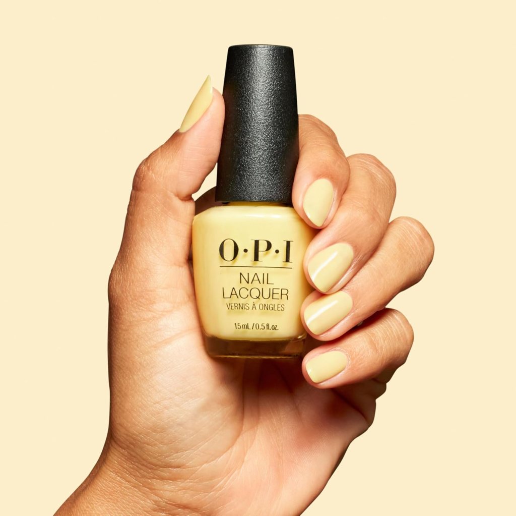 A hand holding a bottle of O.P.I nail lacquer with a yellow shade, displaying perfectly manicured nails painted in the same color.