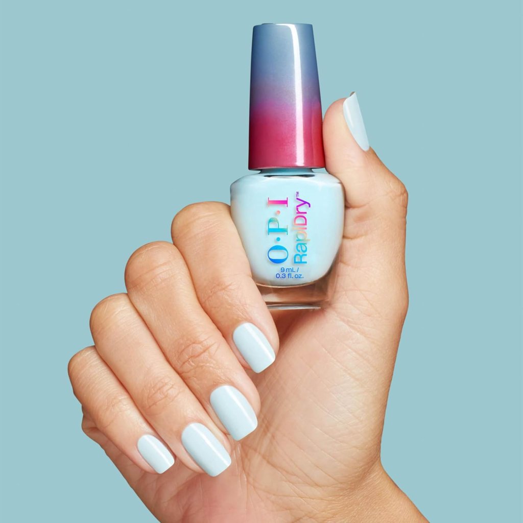 A hand holding a bottle of O.P.I. RapidDry nail polish, with light blue nail polish applied on the nails, against a solid light blue background.