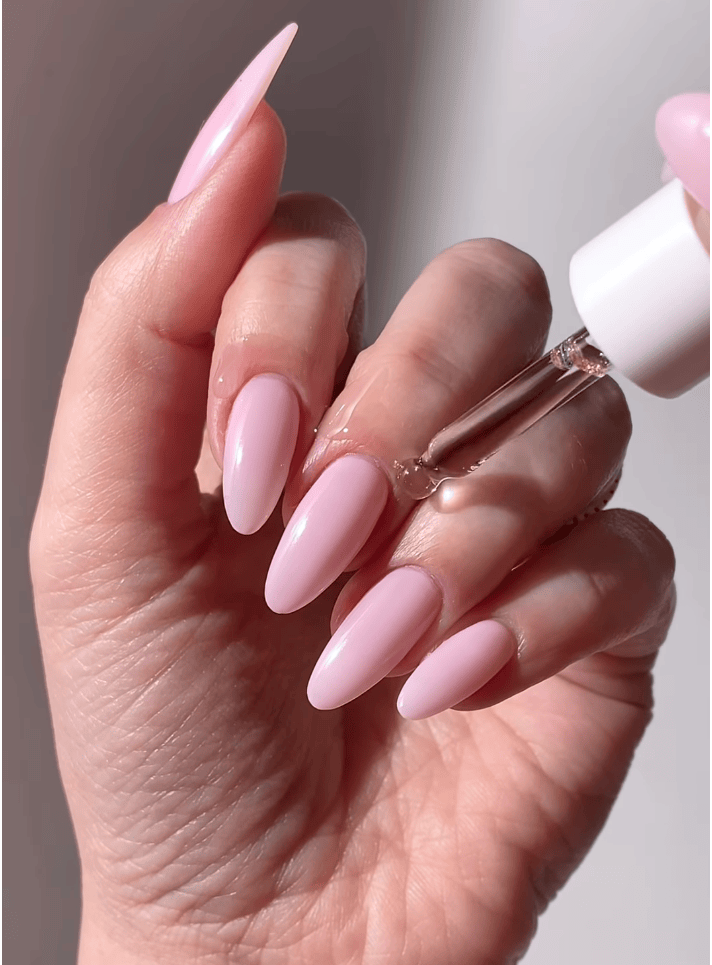 A hand holding a dropper bottle with clear liquid, showcasing long, neatly manicured pink nails.